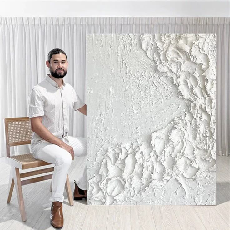 a man sitting on a chair in front of a white wall