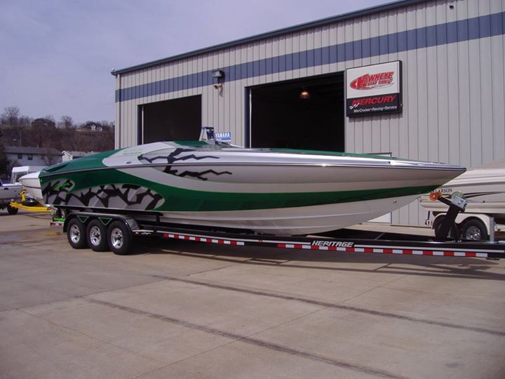 a green and white boat is being towed by a trailer in front of a building