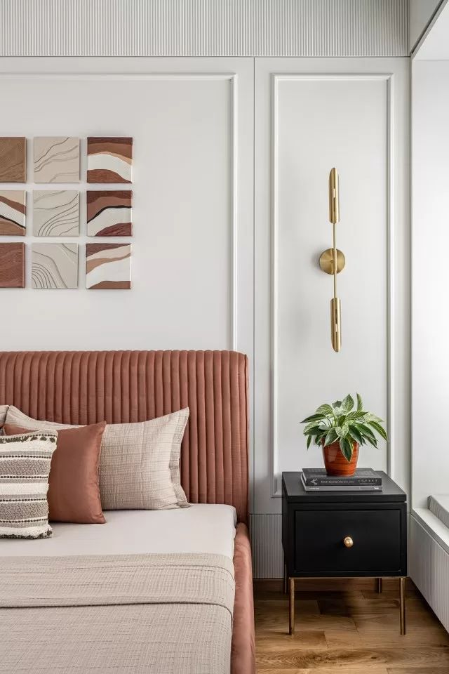 a bed sitting next to a wall with paintings on it's walls and a plant in the corner