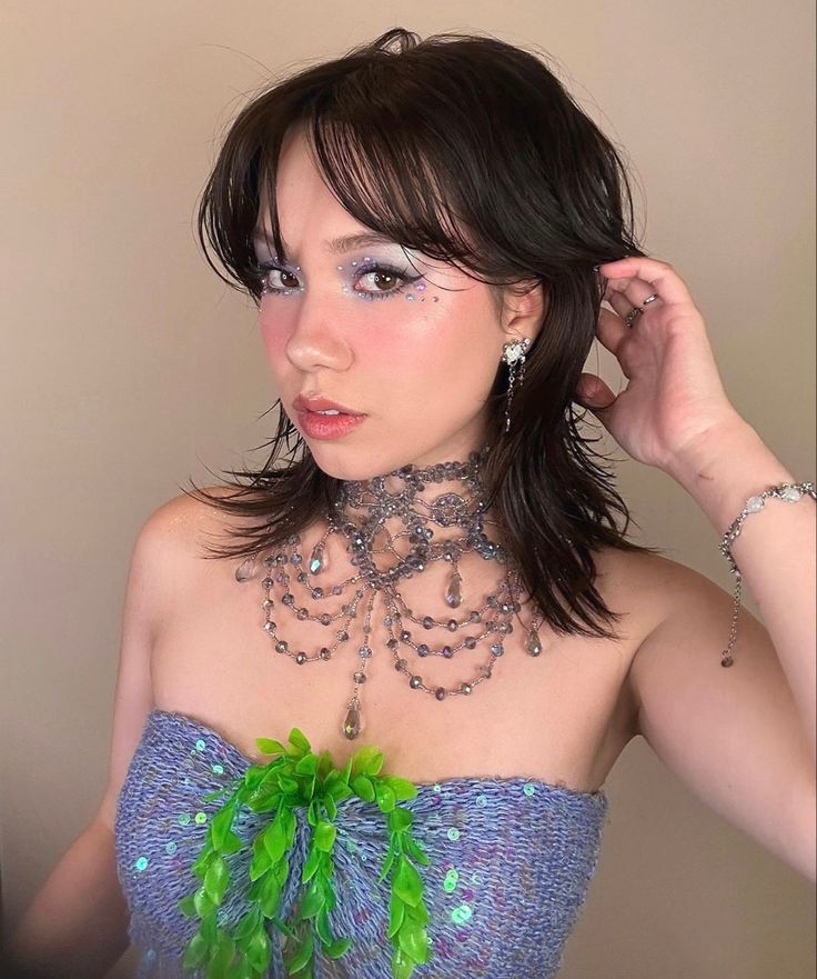 a woman in a blue dress with green feathers on her neck and beads around her neck