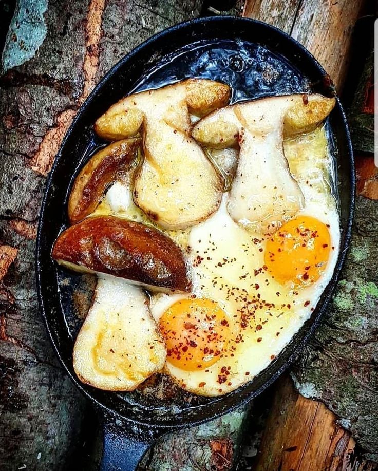 an egg and sausage breakfast in a cast iron skillet on top of a tree trunk