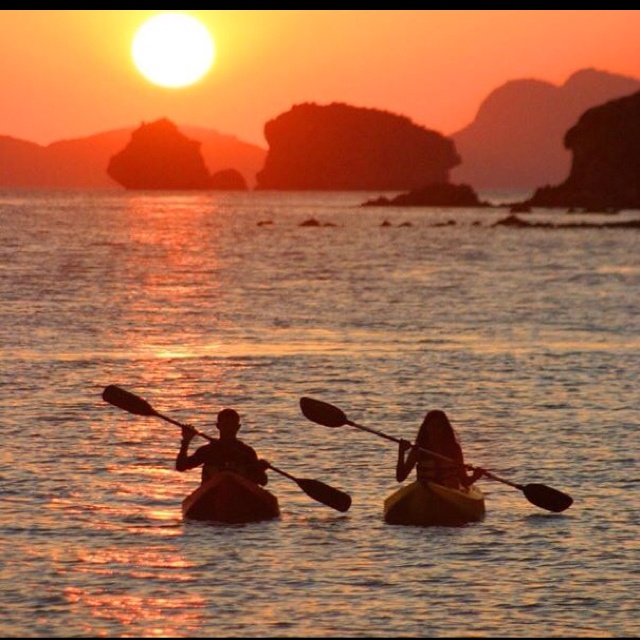 two people are kayaking in the ocean at sunset