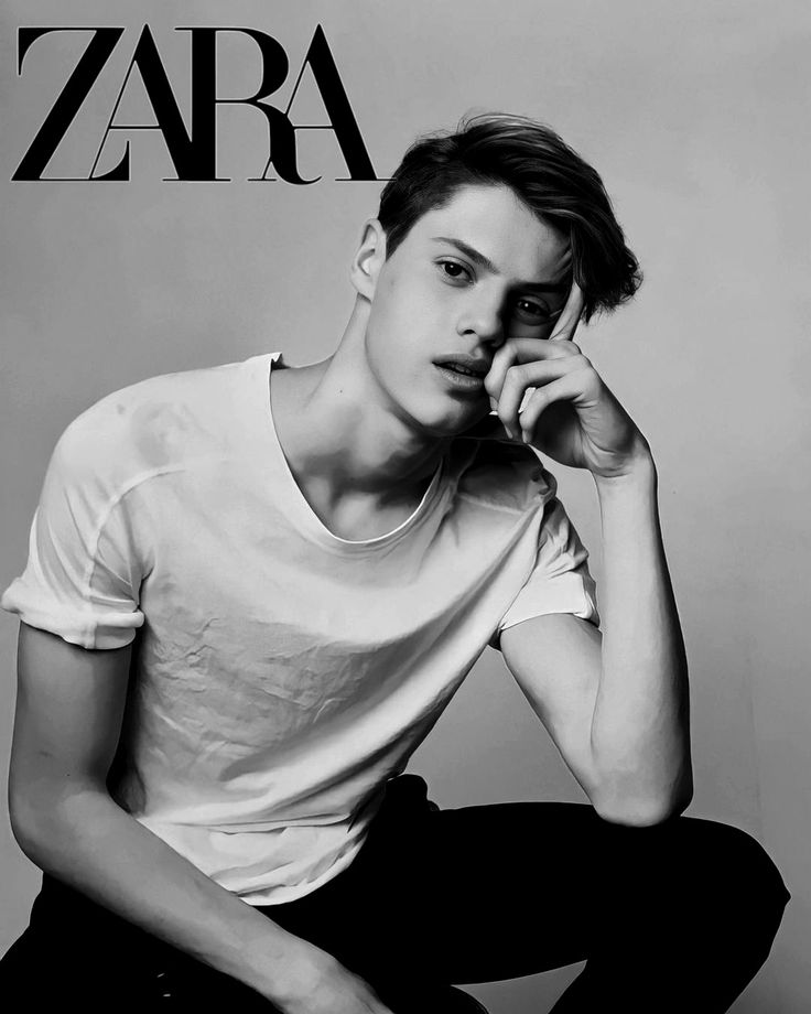 a young man sitting on the floor with his hand to his face while wearing a white t - shirt and black pants