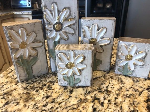 four white and gold flower blocks sitting on top of a granite countertop in a kitchen