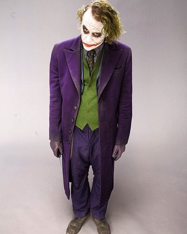 a man dressed as the joker standing in front of a gray background