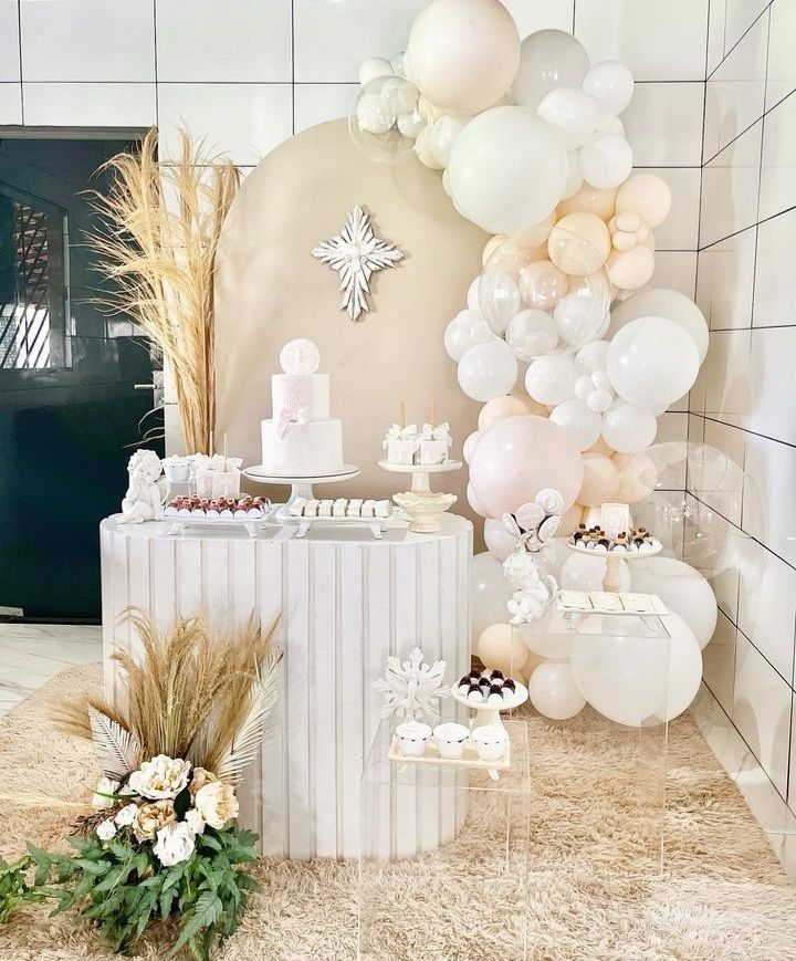 a table topped with lots of balloons next to a wall filled with white and pink decorations