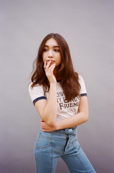 a young woman posing with her hands on her mouth while wearing jeans and a t - shirt