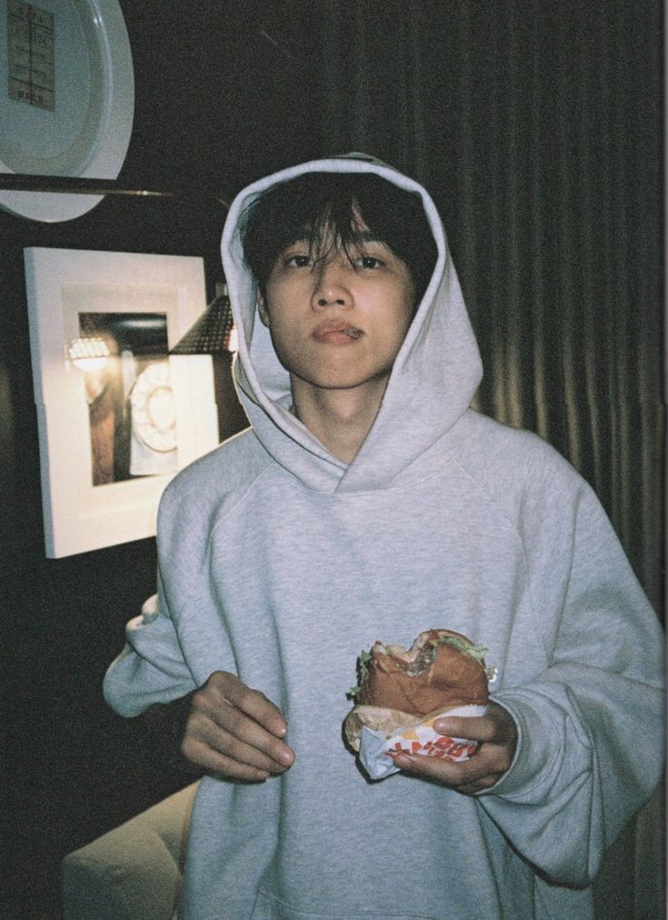 a young man in a hoodie holding a sandwich and looking up at the camera