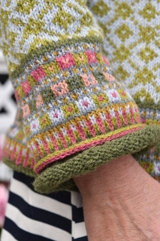 a close up of a person's hand wearing a knitted sweater and striped shirt