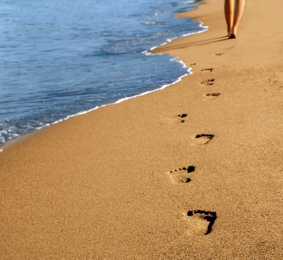 a person walking on the beach with their footprints in the sand and water behind them