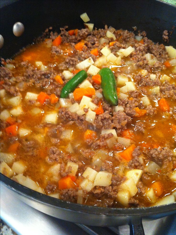 a pan filled with meat and vegetables cooking on top of a stove burner next to a green pepper