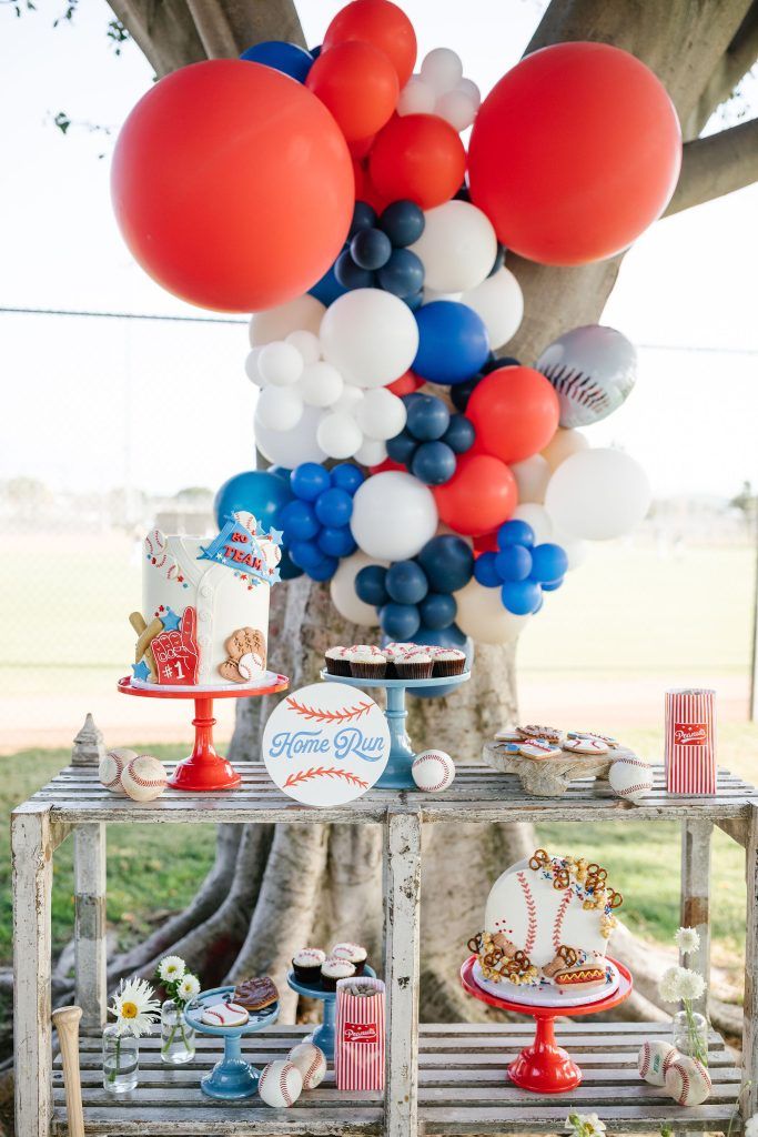 a baseball themed party with balloons and desserts on a wooden table in front of a tree