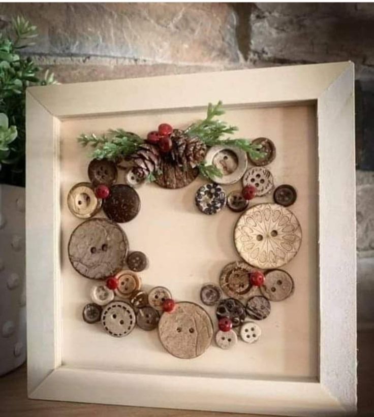 a white frame with buttons and pine cones in the shape of a wreath on it