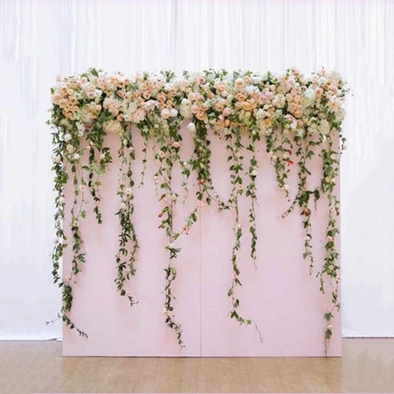 an arrangement of flowers and greenery is displayed on the side of a pink wall