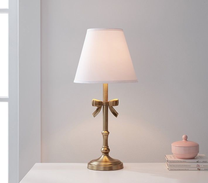 a lamp that is on top of a white table next to a book and cup