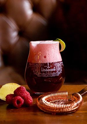 a glass filled with liquid sitting on top of a table next to raspberries