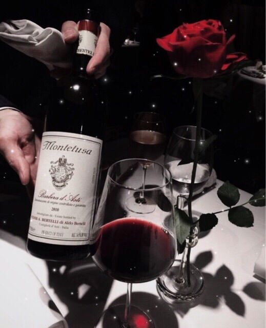 a person pouring wine into a glass on top of a table next to a rose