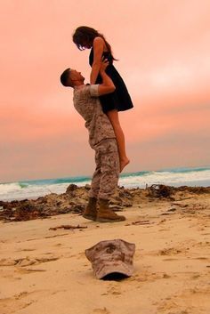 a man and woman standing on top of a sandy beach next to the ocean at sunset