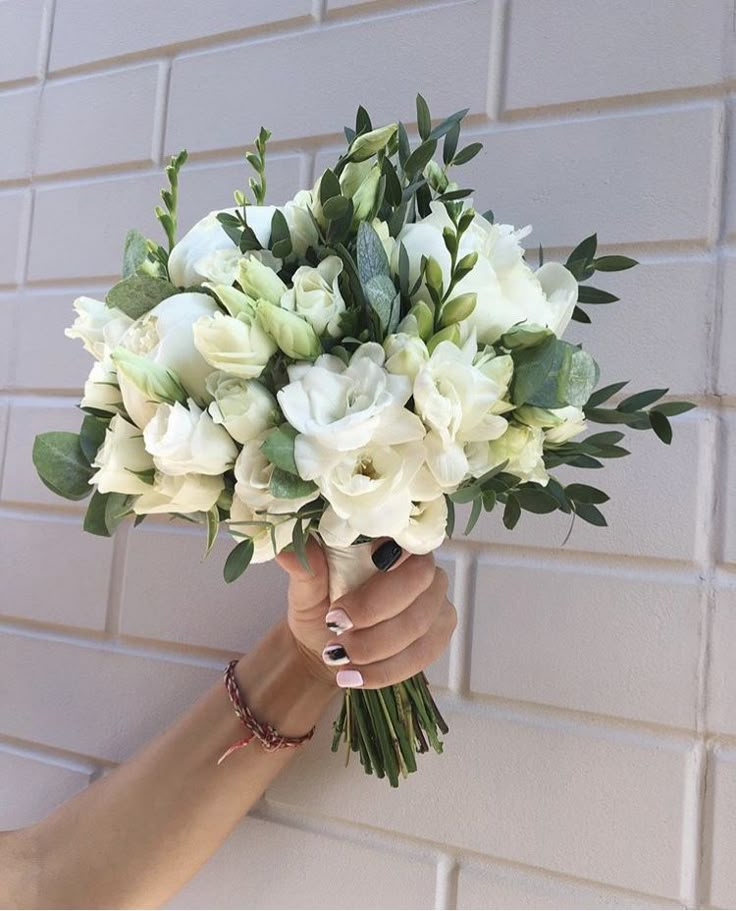 a woman holding a bouquet of white flowers in her left hand against a brick wall