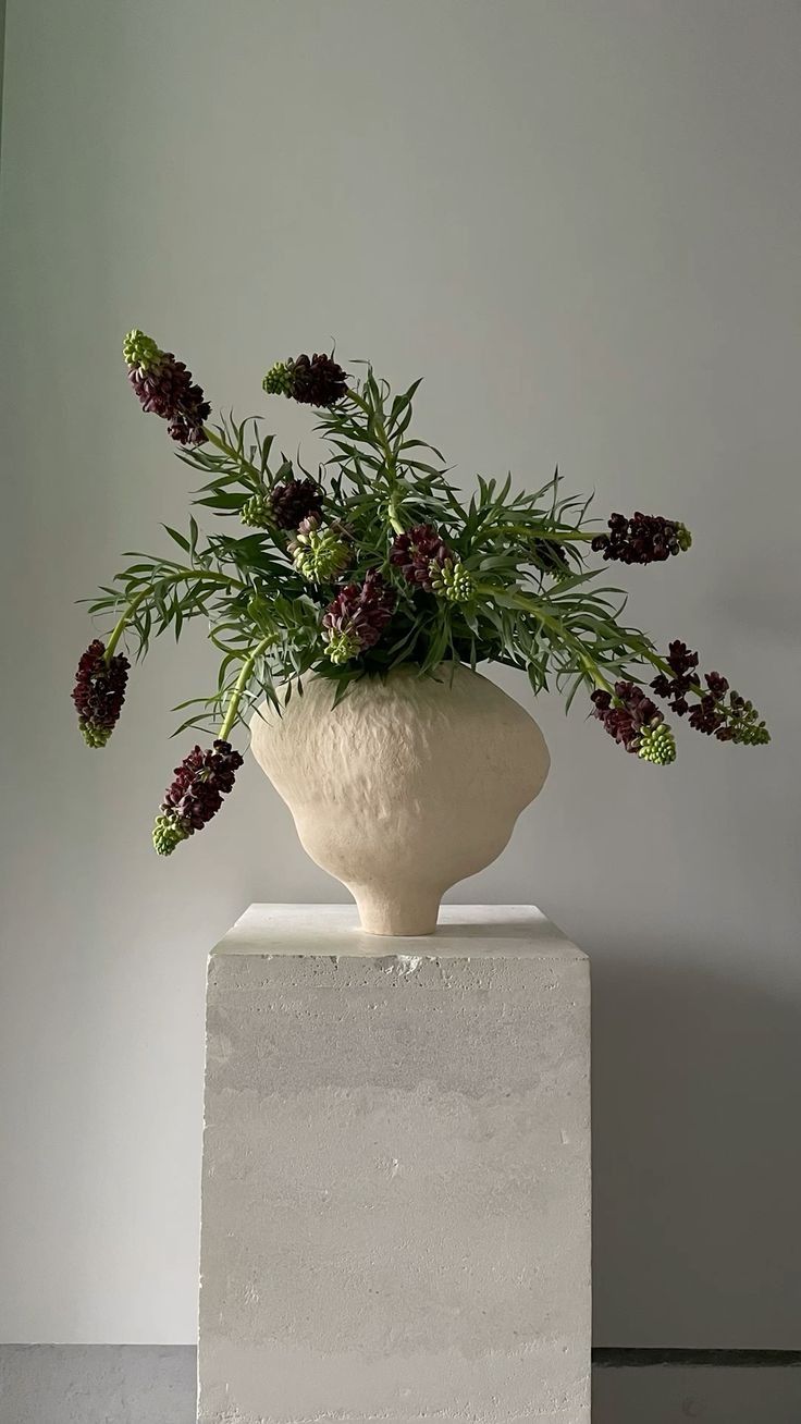 a white vase filled with lots of flowers on top of a block of concrete next to a wall