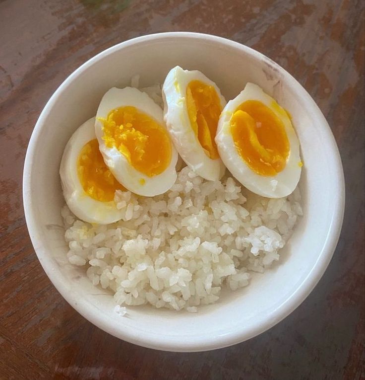 three boiled eggs sit on top of rice in a white bowl atop a wooden table