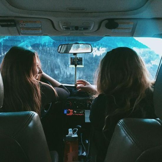 two women sitting in the back seat of a car looking out at mountains and trees