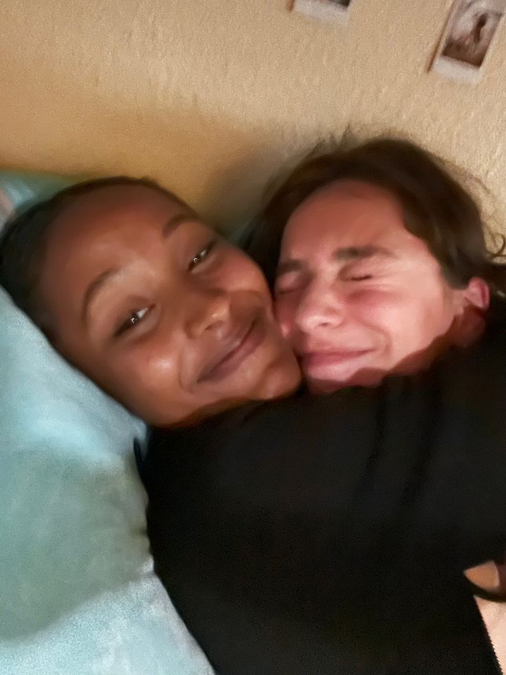 two women laying on top of a bed next to each other with their arms around one another