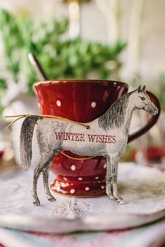 a white horse figurine sitting on top of a table next to a red cup