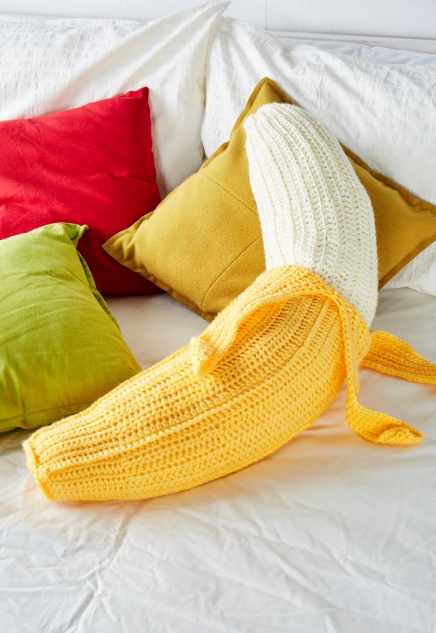 a banana is laying on the bed with four different colored pillows in front of it