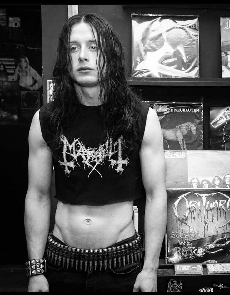 a man with long hair and no shirt standing in front of some recordshelves