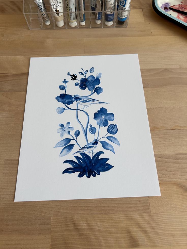 a paper with blue flowers on it sitting on a table next to some paint brushes