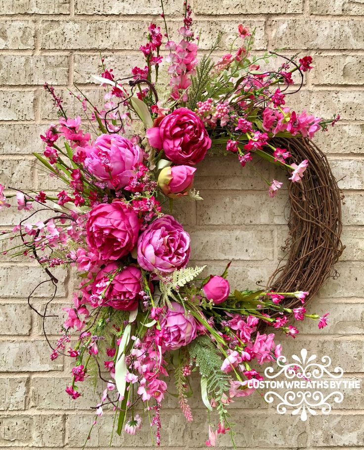 a wreath with pink flowers hanging on a brick wall