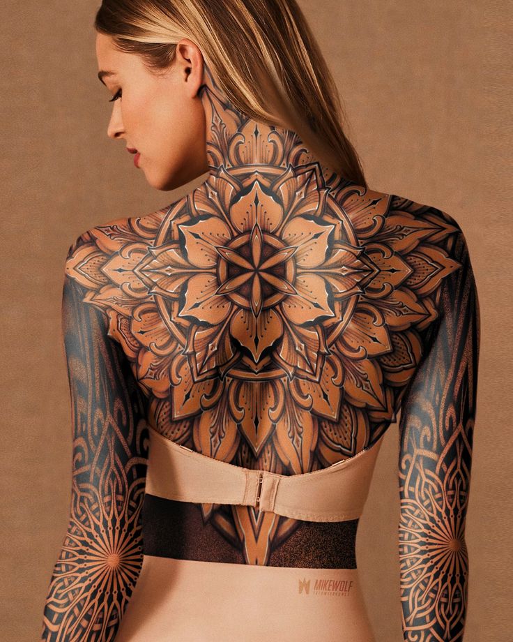 a woman with tattoos on her back and arms is standing in front of a brown background