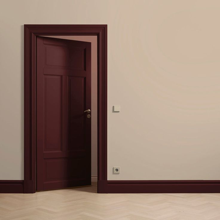 an empty room with a red door and wooden floor, in front of a white wall