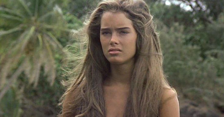 a woman with long hair and no shirt standing in front of palm trees looking at the camera