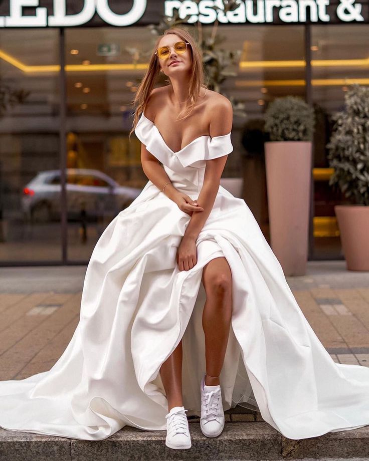 a woman in a white dress is sitting on a ledge outside a restaurant and posing for the camera