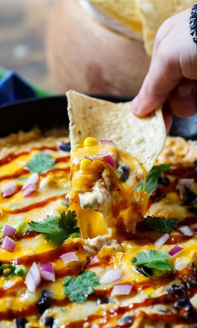 a person dipping a tortilla chip into a skillet filled with mexican food