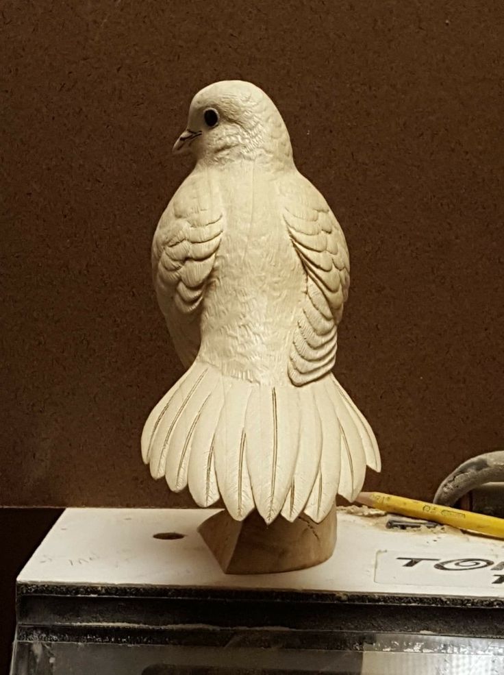 a white bird statue sitting on top of a box next to a yellow pencil and ruler