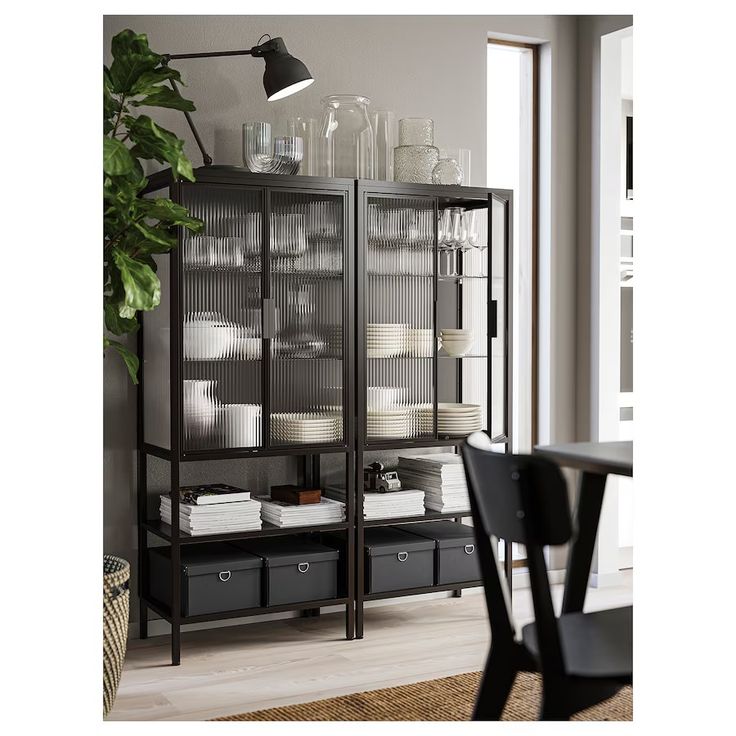 a black bookcase with glass doors and drawers in front of a dining room table