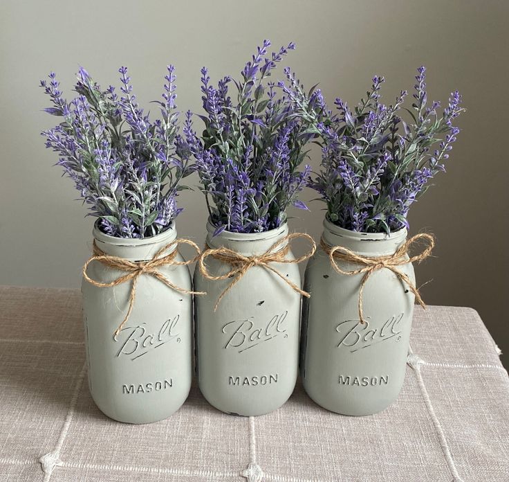 three mason jars with lavenders tied to them are sitting on a linen tablecloth