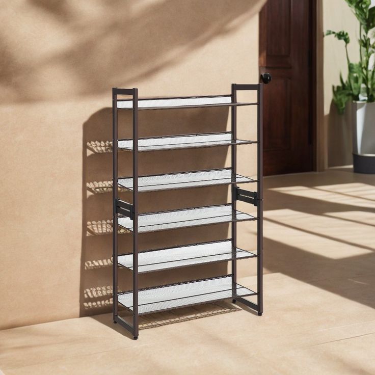 a metal shelf with several shelves on the side of a building next to a potted plant