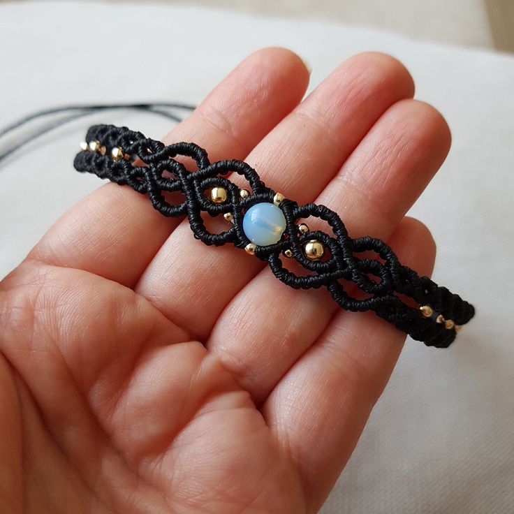 a hand holding a black string bracelet with a blue bead and gold beads on it