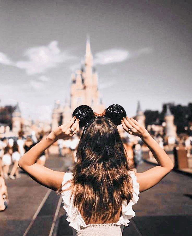 a woman is standing in front of a castle with minnie ears on her head looking at the sky