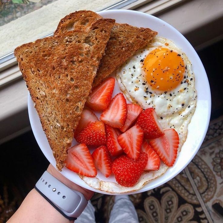 a person holding a plate with toast, strawberries and an egg