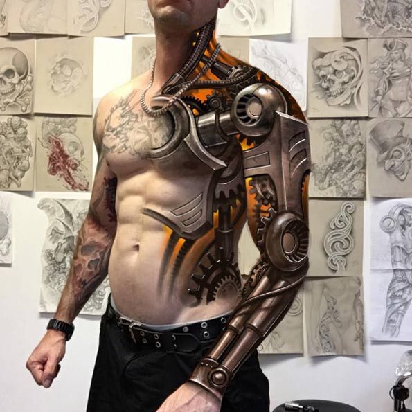 a man standing in front of a wall with tattoos on his chest and arms, holding a mechanical arm