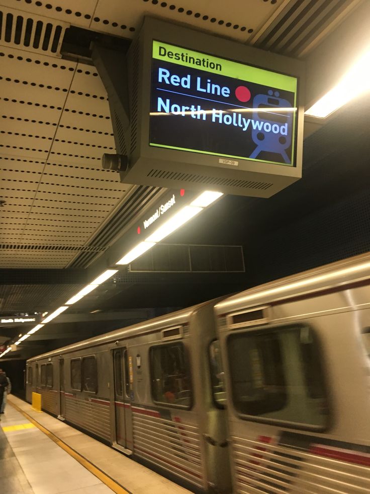 a silver train traveling past a station next to a sign that says red line north hollywood