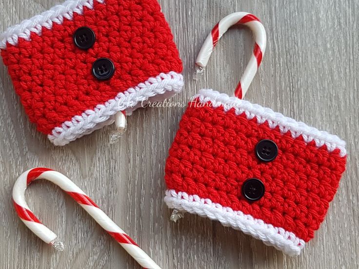 two red and white crocheted cups with candy canes next to them on a table