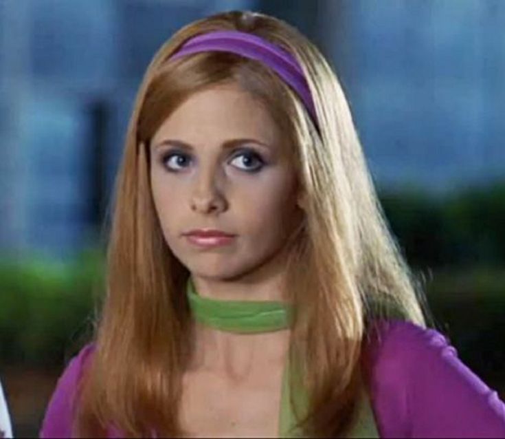 a woman with long red hair wearing a purple top and green collar around her neck