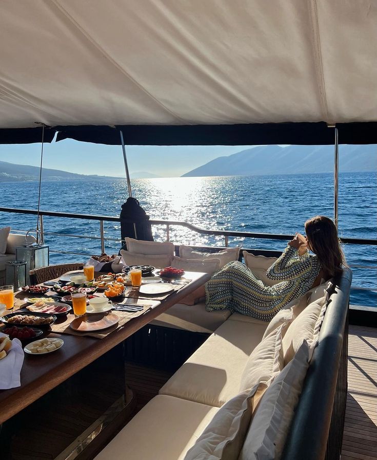 a woman sitting at a table on top of a boat with food and drinks in front of her