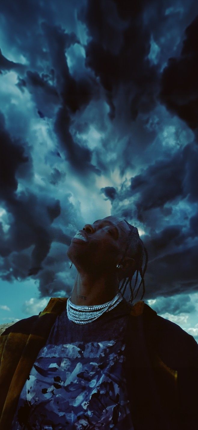 a man with dreadlocks standing in front of a cloudy sky and looking up at the sky